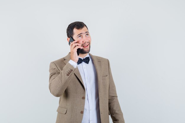 Jong mannetje in pak dat op mobiele telefoon spreekt en vrolijk, vooraanzicht kijkt.