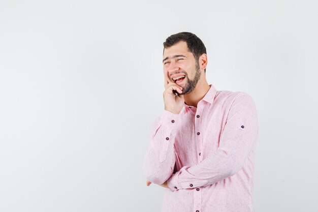 Jong mannetje in roze overhemd dat terwijl hij zijn kin vasthoudt en gelukkig kijkt