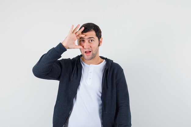 Jong mannetje in t-shirt, jasje dat door vingers kijkt en zelfverzekerd, vooraanzicht kijkt.