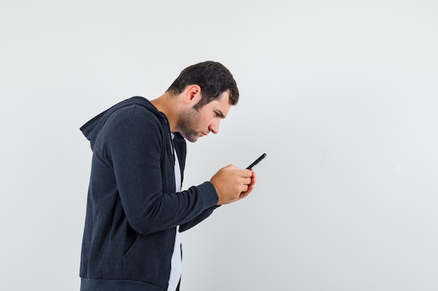 Jong mannetje in t-shirt, jasje met behulp van mobiele telefoon en gericht kijken.