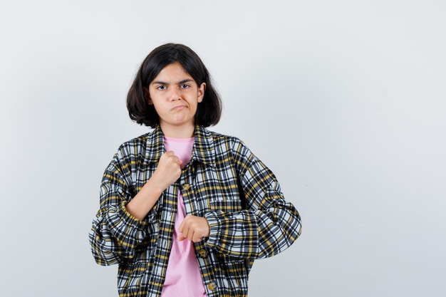 Jong meisje balde vuisten in geruit overhemd en roze t-shirt en kijkt boos.