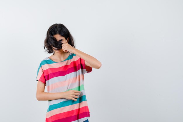 Jong meisje bedekt gezicht met haar in kleurrijk gestreept t-shirt en ziet er schattig uit, vooraanzicht.