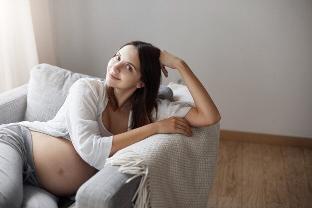 Jong meisje blij zwanger te zijn. Thuis blijven op een warme en gezellige bank met een deken.