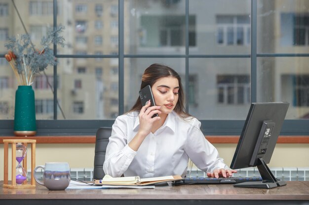 Jong meisje dat aan de telefoon praat terwijl ze op de pc werkt Foto van hoge kwaliteit