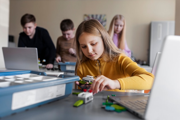 Jong meisje dat een laptop en elektronische onderdelen gebruikt om een robot te bouwen