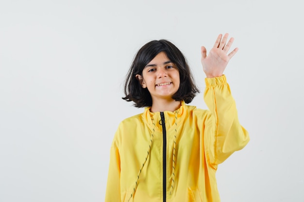 Gratis foto jong meisje dat hand opheft als iemand in geel bomberjack groet en gelukkig kijkt