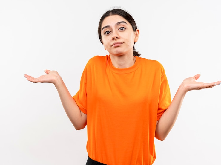 Gratis Foto jong meisje dat oranje t-shirt draagt verward schouderophalend schouders die geen antwoord hebben die zich over witte muur bevinden