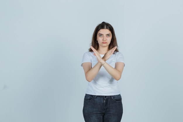 Jong meisje dat stopgebaar in t-shirt, jeans toont en ernstig kijkt. vooraanzicht.