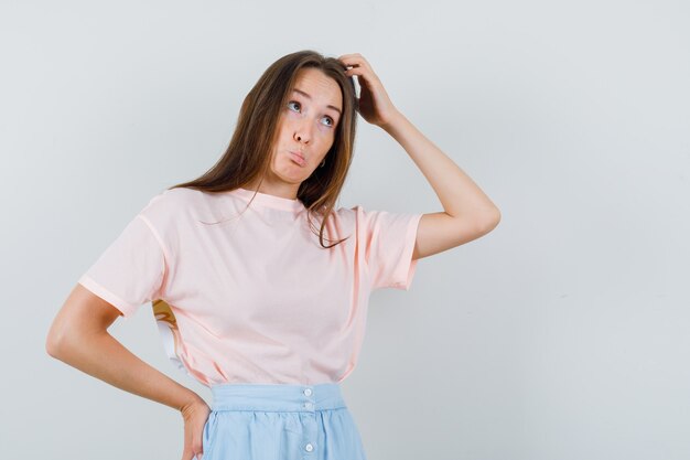 Jong meisje hoofd in t-shirt, rok krabben en aarzelend, vooraanzicht op zoek.