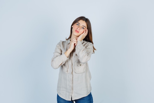 Jong meisje in beige shirt, jeans leunend op de handpalm en ziet er aantrekkelijk uit, vooraanzicht.