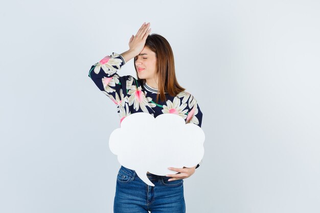 Jong meisje in bloemen blouse, jeans met hand op het hoofd en boos kijken, vooraanzicht.