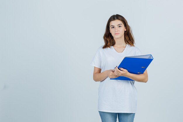 Jong meisje in de witte map van de t-shirtholding en op zoek verstandig, vooraanzicht.