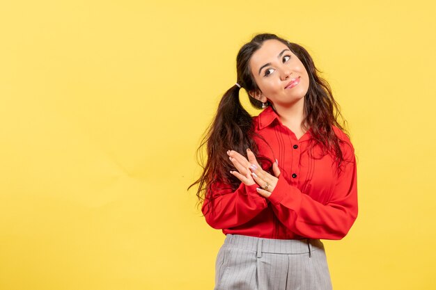 jong meisje in een rode blouse glimlachend en klappen op geel