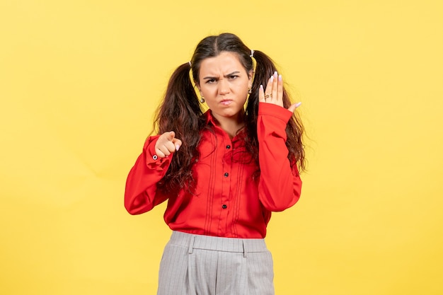 jong meisje in een rode blouse met een boos gezicht op geel