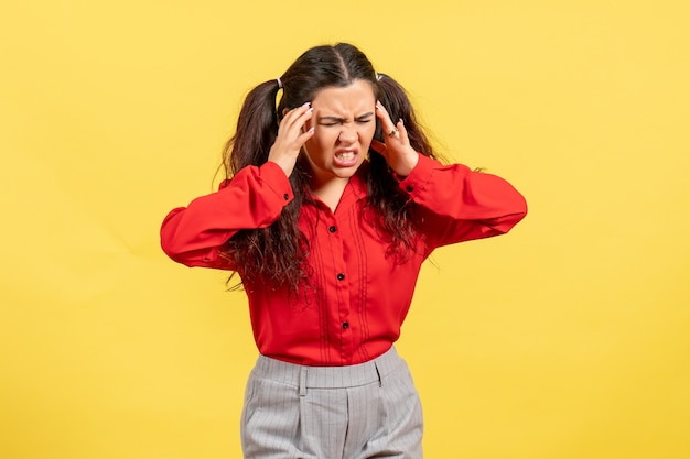 Gratis foto jong meisje in een rode blouse met hoofdpijn op geel