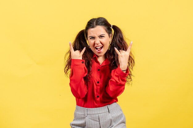 jong meisje in een rode blouse poseren met emotioneel gezicht op geel