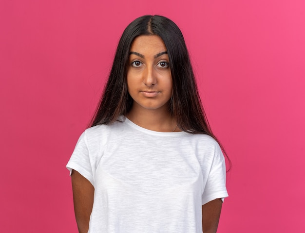 Jong meisje in een wit t-shirt dat naar de camera kijkt met een serieuze zelfverzekerde uitdrukking die over roze staat