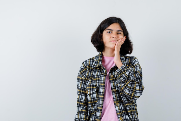 Jong meisje in geruit overhemd en roze t-shirt hand op de wang zetten en peinzend kijken, vooraanzicht.