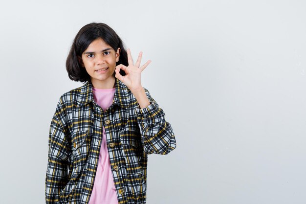 Jong meisje in geruit overhemd en roze t-shirt met ok teken en schattig, vooraanzicht.