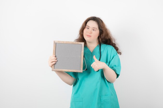 jong meisje in groen uniform met een frame met een duim omhoog. vrouw