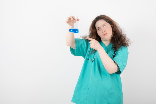 jong meisje in groen uniform wijzend op een glazen pot met blauwe vloeistof.