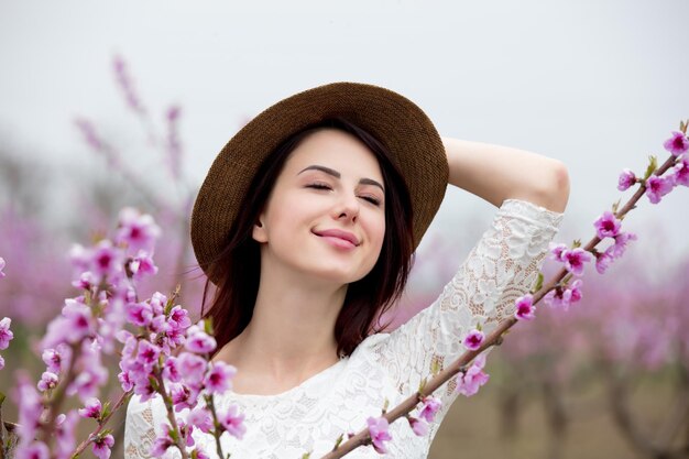 Jong meisje in hoed in de buurt van bloesem perzikboom in een lentetuin.