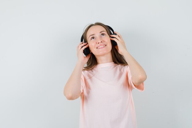 Jong meisje in roze t-shirt genieten van muziek met koptelefoon en op zoek vrolijk, vooraanzicht.
