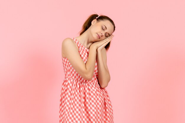 jong meisje in schattige lichte jurk moe voelt en probeert te slapen op roze