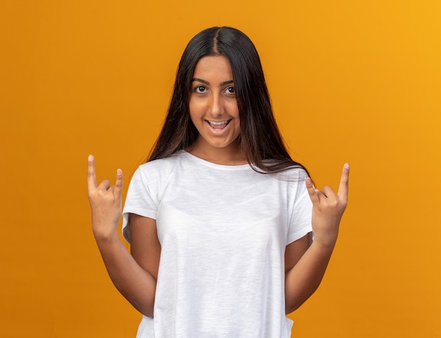 Jong meisje in wit t-shirt kijken camera blij en vrolijk met rock symbool