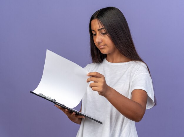 Jong meisje in wit t-shirt met klembord met blanco pagina's die er met een serieus gezicht naar kijken