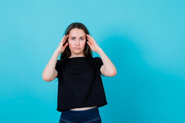 Jong meisje kijkt naar de camera door handen vast te houden op tempels op blauwe achtergrond