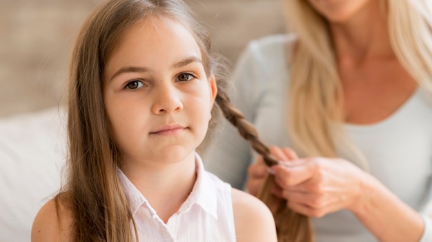 Jong meisje krijgt haar haar gevlochten door haar moeder