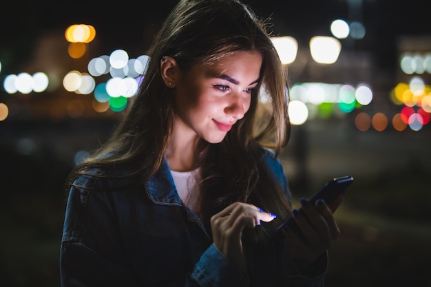 Jong meisje met behulp van digitale tablet op de lichte bokeh van de schoonheid van de nacht in de stad
