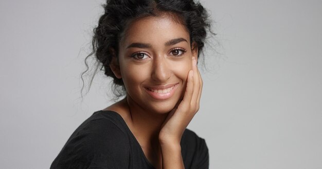 Jong meisje met een perfecte lichtbruine huid en mooi krullend zwart haar glimlachend naar de camera in de studio