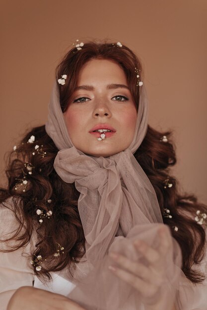 Jong meisje met groene ogen houdt kleine bloem vast met haar tanden Dame in hoofddoek poseert met bloemen in krullend haar