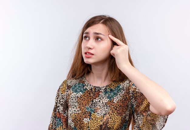 Jong meisje met lang haar dat kleurrijke kleding draagt die haar tempel richt die zich probeert te herinneren