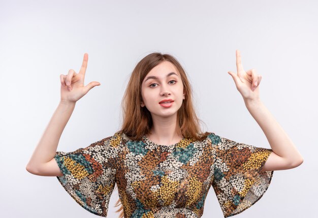 Jong meisje met lang haar dat kleurrijke kleding draagt die wijsvingers met ernstige zekere uitdrukking op gezicht omhoog richt