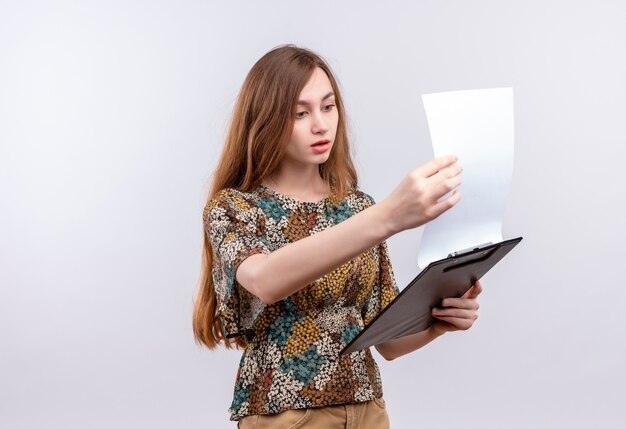 Jong meisje met lang haar die het kleurrijke klembord van de kledingsholding dragen die blanco pagina's bekijkt