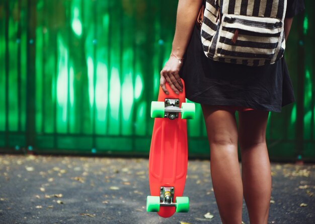 Jong meisje met plastic oranje stuiver shortboard achter groene muur in cap