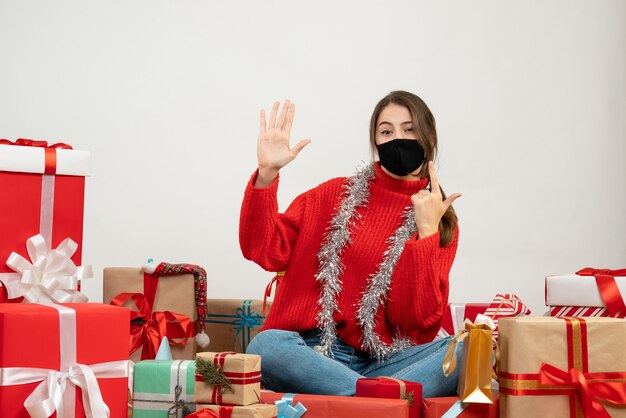 jong meisje met rode trui en zwart masker pistool teken rondhangen presenteert op wit