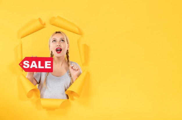 Jong meisje met verkoop inscriptie teken op gescheurde gele papieren achtergrond indoor gezichtsbehandeling
