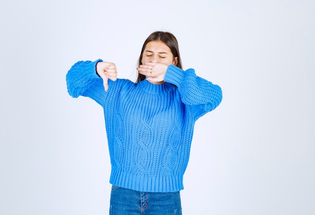 jong meisje model in blauwe trui geeuwen en met een duim naar beneden.