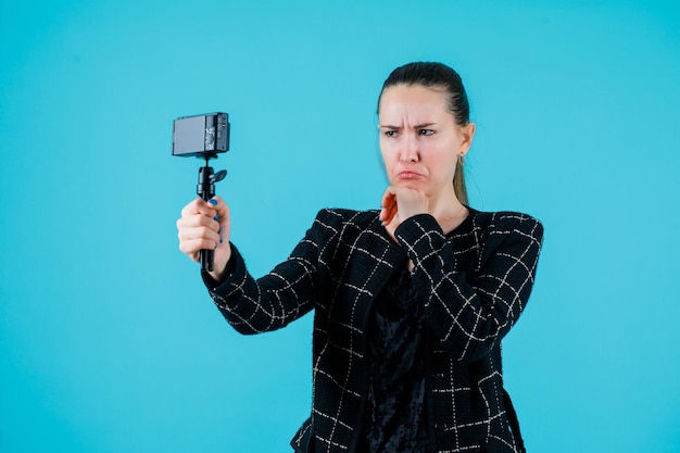 Jong meisje neemt selfie door huilende mimiek op blauwe achtergrond te tonen
