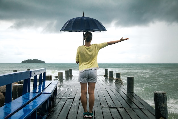 jong meisje op pier met paraplubakken met zijn rug naar de zee