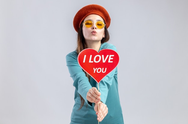 Jong meisje op valentijnsdag dragen hoed met bril stak rood hart op een stokje met ik hou van je tekst op camera weergegeven: kus gebaar geïsoleerd op witte achtergrond