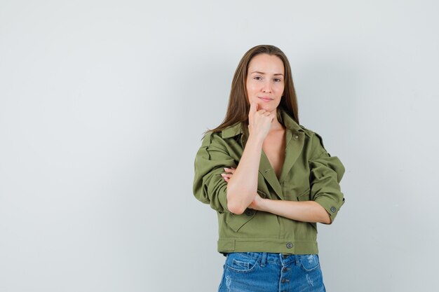 Jong meisje permanent in denken pose in jas, korte broek en op zoek verstandig, vooraanzicht.