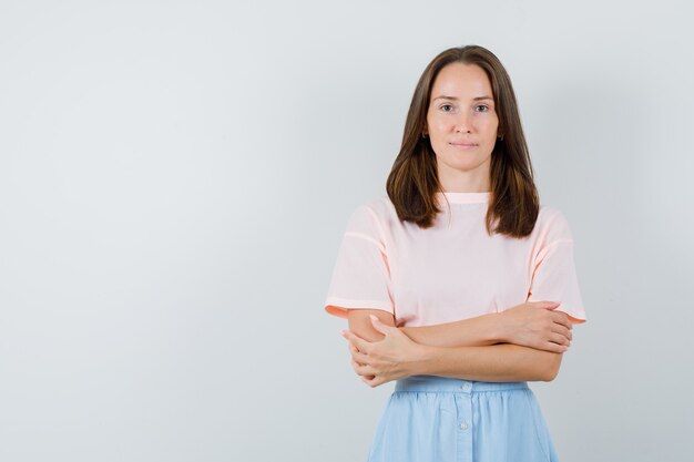 Jong meisje permanent met gekruiste armen en glimlachend in t-shirt, rok vooraanzicht.