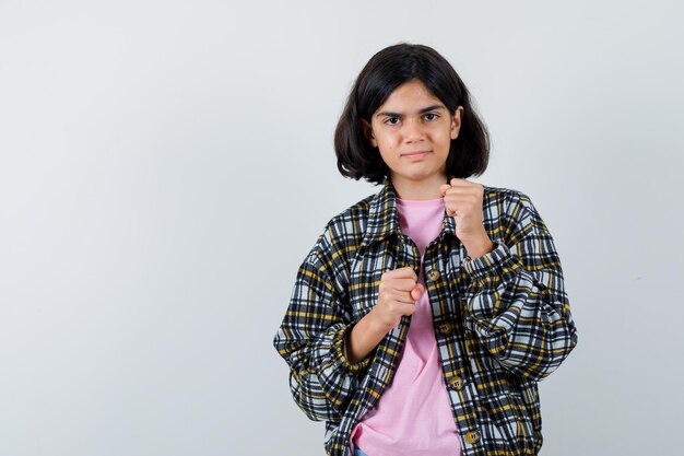 Jong meisje staat in boxer pose in geruit overhemd en roze t-shirt en ziet er schattig uit.