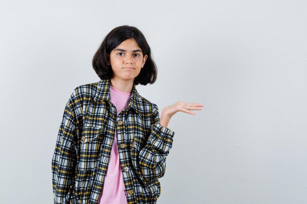 Jong meisje strekt zich uit met de palm in geruit overhemd en roze t-shirt en ziet er schattig uit. vooraanzicht.