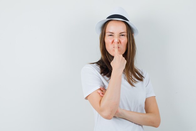 Gratis foto jong meisje wat betreft neus met vinger in witte t-shirthoed